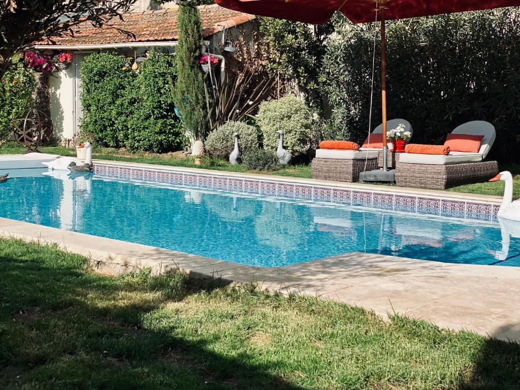 a swimming pool with two chairs and an umbrella at Villa Maskali in Cuxac-dʼAude