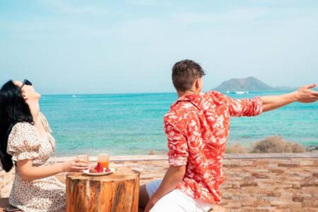 a man and a woman sitting next to the ocean at Corralejo Beach Villa San Antonio- Private Heated Pool, Breathtaking Sea View, BBQ, Fast Wifi by Amazzzing Travel in Corralejo