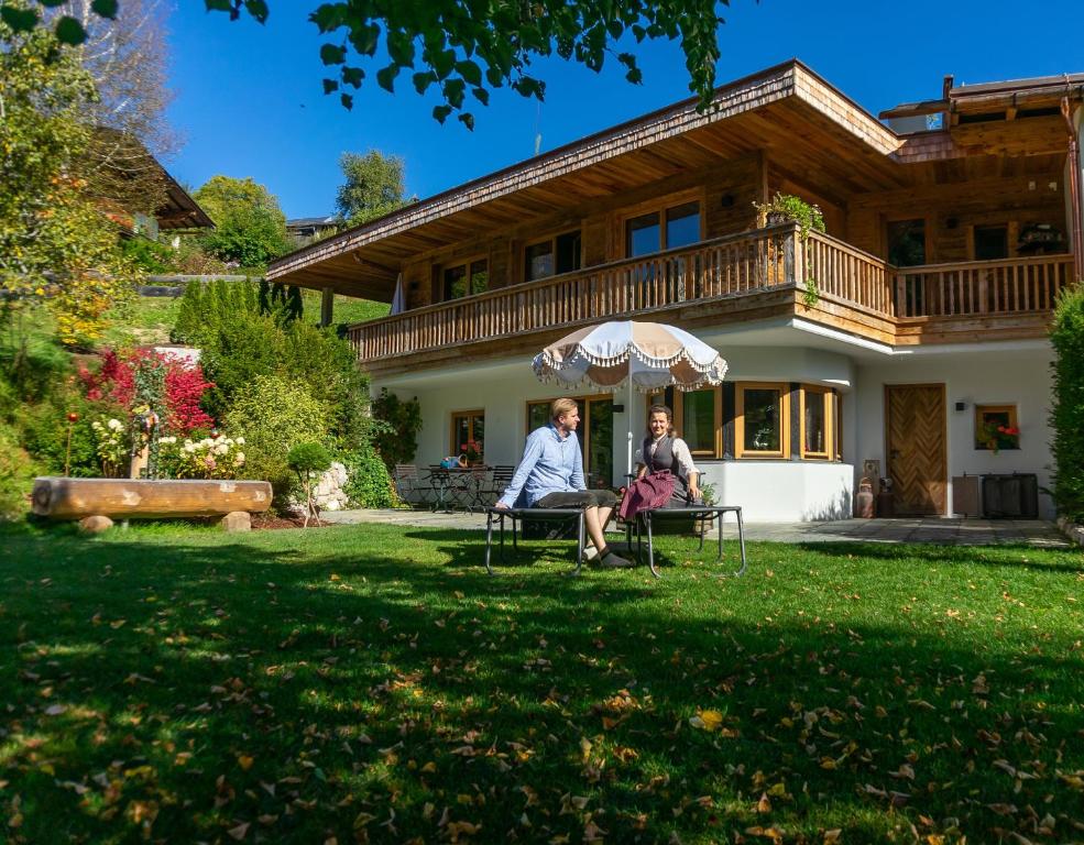 zwei Personen, die unter einem Schirm vor einem Haus sitzen in der Unterkunft CHALET KITZBICHL, your Holiday Hideaway by Belle Stay in Reith bei Kitzbühel