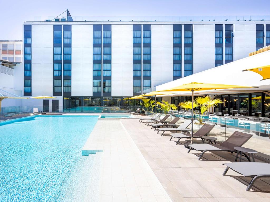 - une piscine avec des chaises et des parasols en face d'un bâtiment dans l'établissement Radisson Hotel Saint Denis, La Reunion, à Saint-Denis