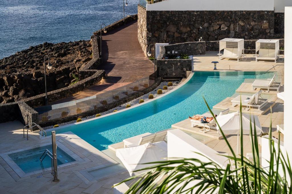 a swimming pool with chairs and the ocean in the background at Royal Marina Suites Boutique Hotel - Adults Only in Puerto Calero