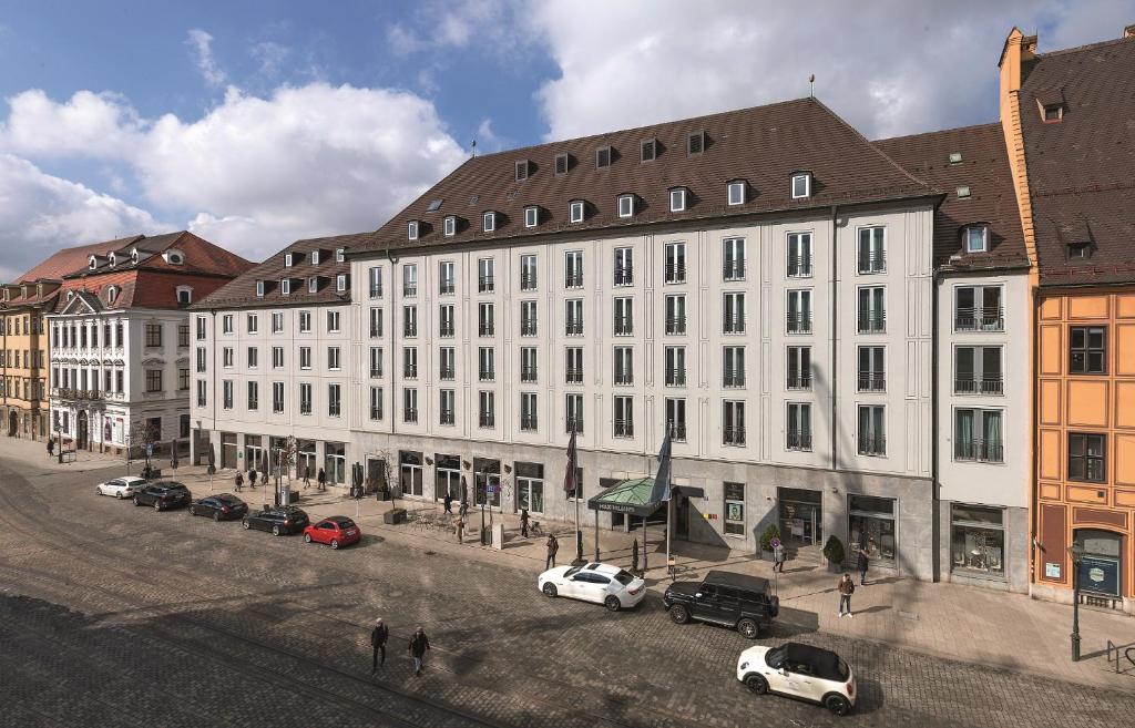 un grand bâtiment blanc avec des voitures garées dans une rue dans l'établissement Hotel Maximilian’s, à Augsbourg