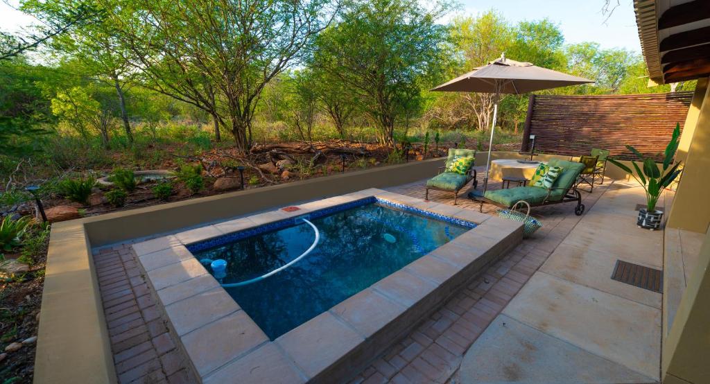 a swimming pool with a table and chairs and an umbrella at Bee-Eater Cottage in Hoedspruit