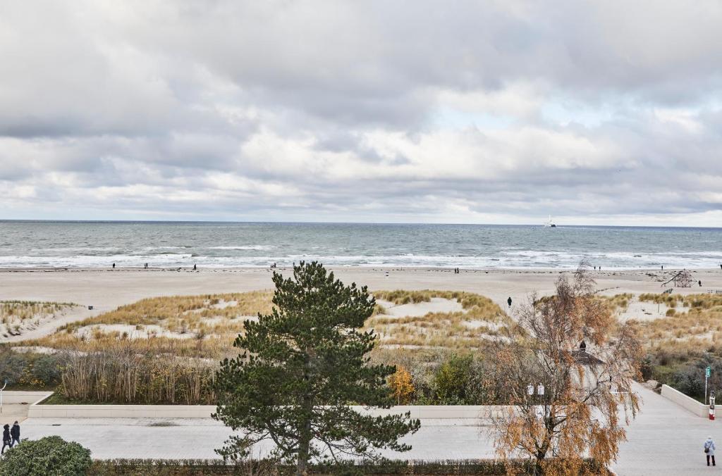 einen Strand mit Menschen, die auf dem Sand und dem Meer wandeln in der Unterkunft Baltic Hideaways Beach Hotel Warnemünde in Warnemünde