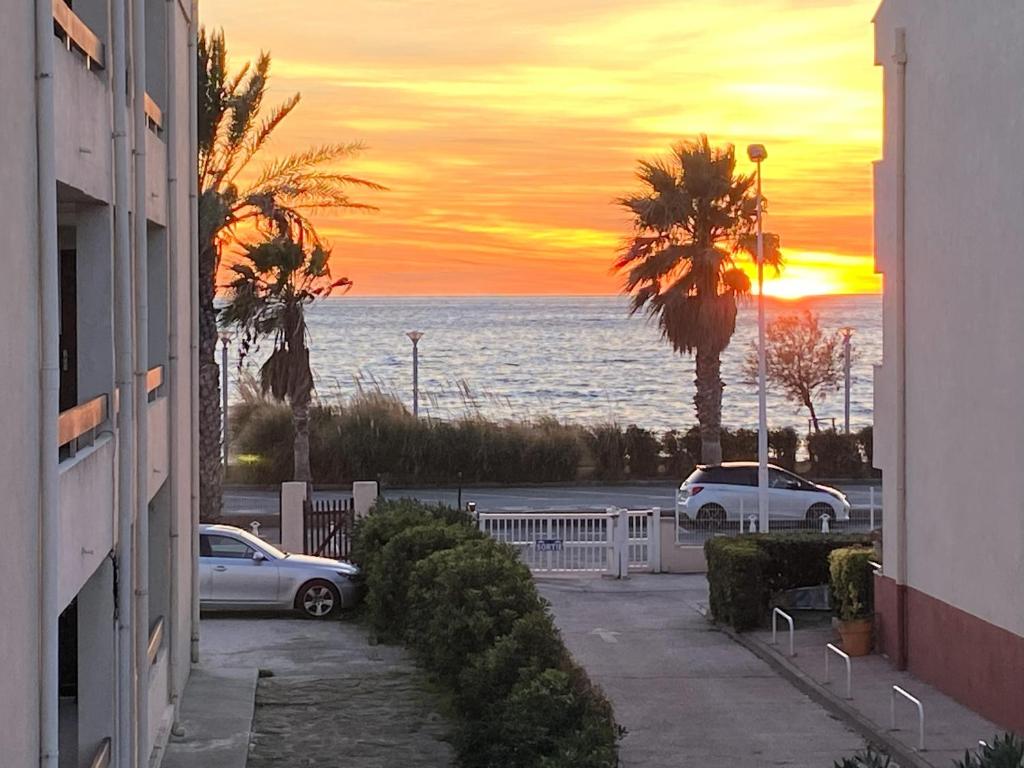 un coucher de soleil sur l'océan avec des voitures garées sur un trottoir dans l'établissement T3 vue mer à 80m de la plage, à Saint-Cyr-sur-Mer