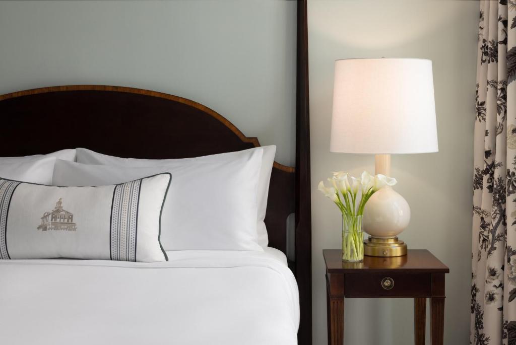 a bed with a lamp and a vase of flowers on a table at The Omni Homestead Resort in Hot Springs