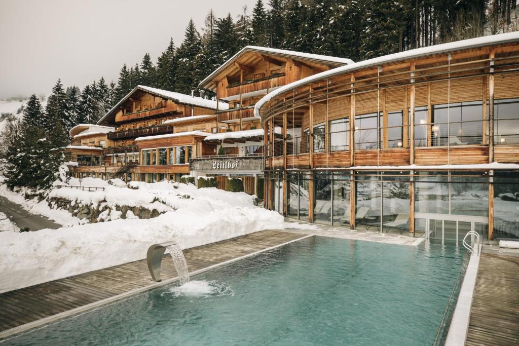 a building with a swimming pool in the snow at Naturhotel Leitlhof in San Candido