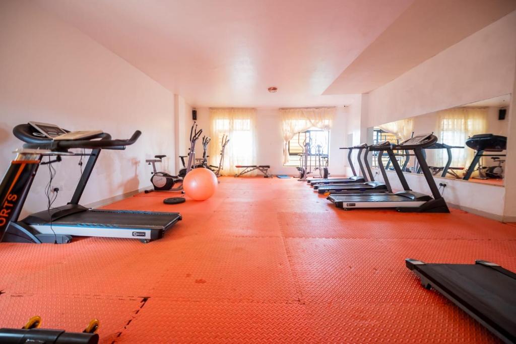 une salle de sport avec plusieurs tapis de course et une rangée de machines dans l'établissement Emerald BnB, à Ruaka