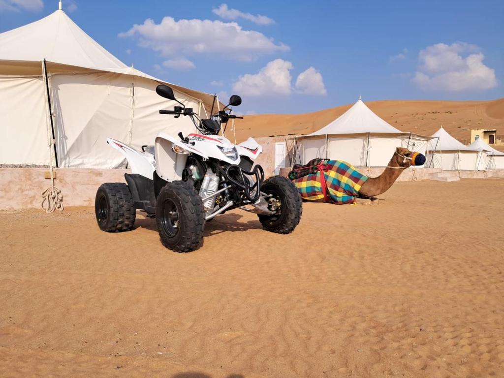 Badīyah的住宿－Al Salam Desert Camp Bidiya，一辆四轮车停在沙漠中,有帐篷