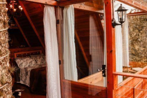 uma porta de vidro para um quarto com uma cama e cortinas em Chalés Recanto do Vale - TUCANO em Bom Jardim da Serra