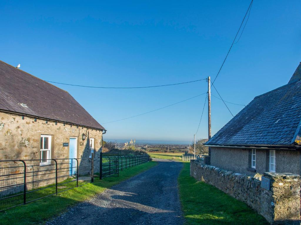 a road between two stone buildings in a field at Plas Bach in Rhoscolyn