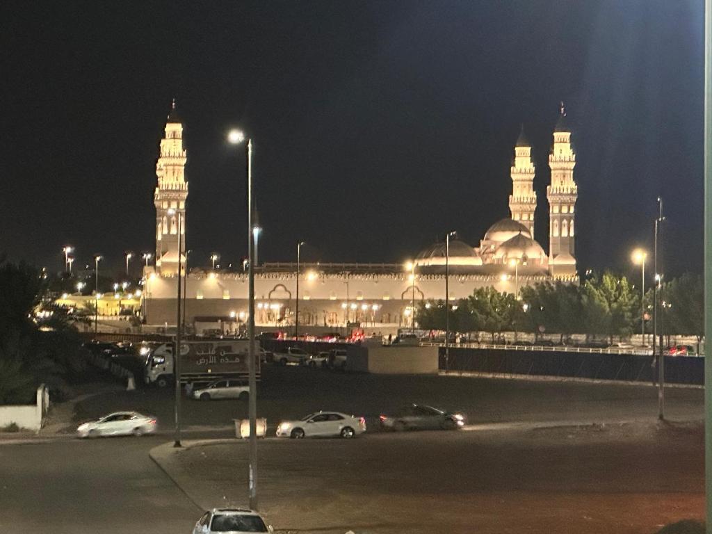 شقق مطله على مسجد قباء في المدينة المنورة: مبنى كبير بالليل وفيه سيارات في موقف