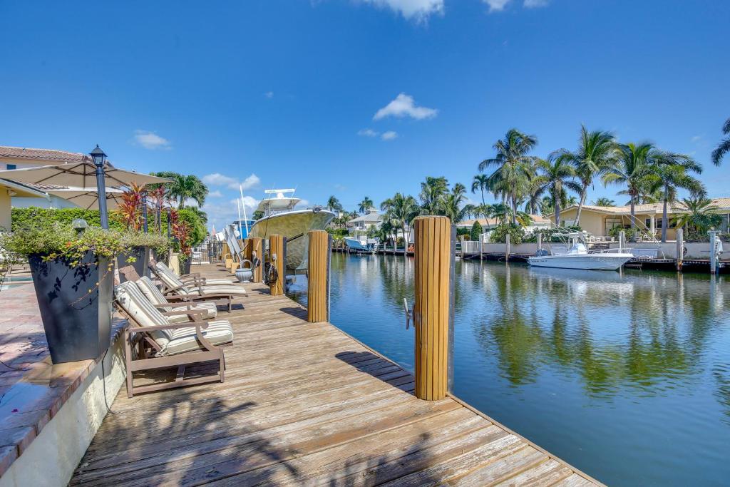 a wooden dock with chairs and a river with houses at Lighthouse Point Home with Pool and Canal Access in Lighthouse Point