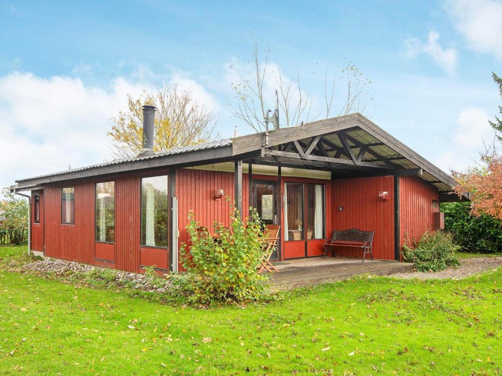 ein rotes Haus mit einer Veranda auf einem grünen Feld in der Unterkunft Holiday home Sydals XXXI in Neder Lysabild
