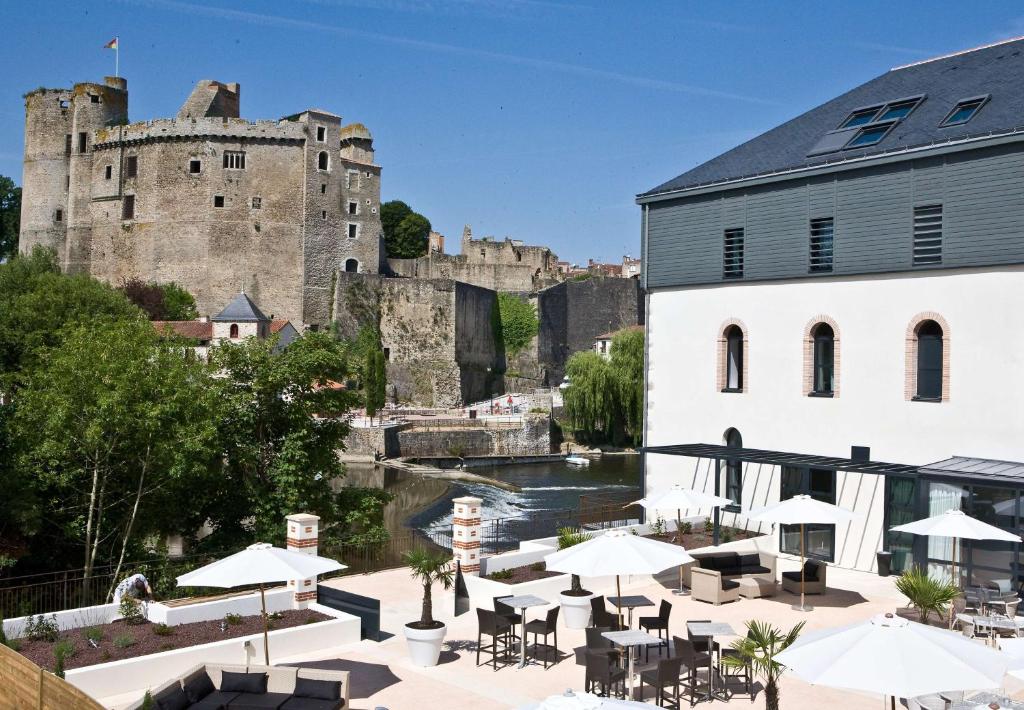 un restaurante con mesas y sombrillas frente a un castillo en Best Western Plus Villa Saint Antoine Hotel & Spa, en Clisson