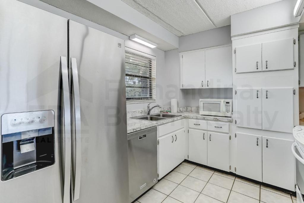 a kitchen with white cabinets and a stainless steel refrigerator at Amelia By The Sea 110 in Fernandina Beach