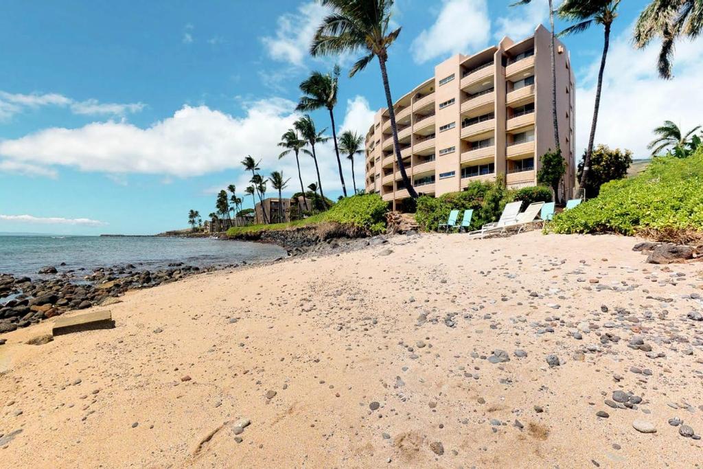 a beach with a building and palm trees and the ocean at Island Sands Resort Condominiums in Wailuku
