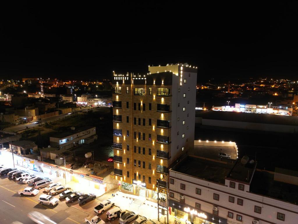 een hoog gebouw met auto's geparkeerd op een parkeerplaats 's nachts bij قمم بارك النماص Qimam Park Hotel 6 in Al Namas