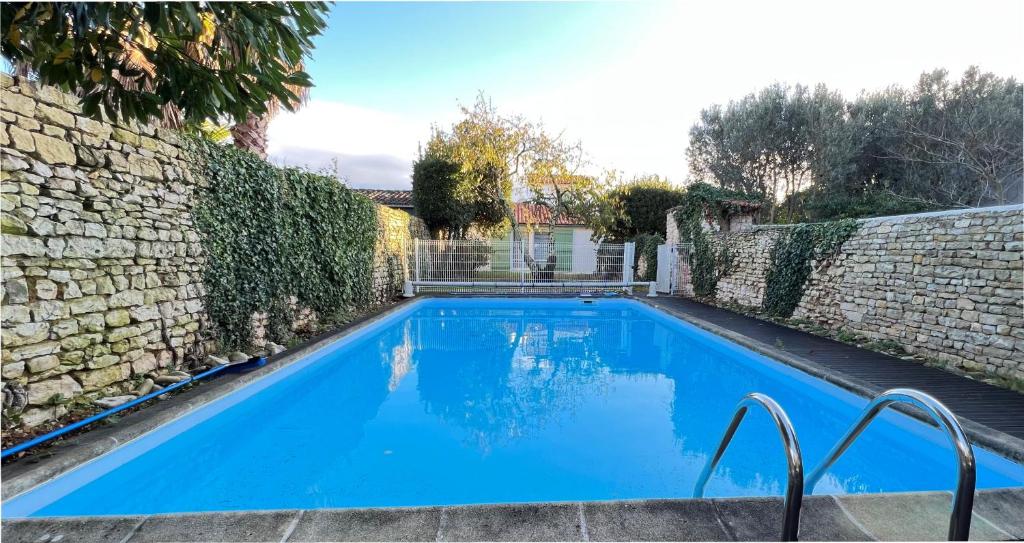ein großer blauer Pool neben einer Steinmauer in der Unterkunft Jolie maison avec jardin, piscine et parking in Sainte-Marie-de-Ré