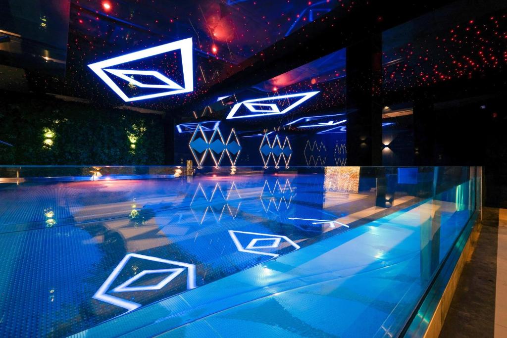 Indoor illuminated pool with geometric LED ceiling lights reflecting on calm blue water, modern ambiance.