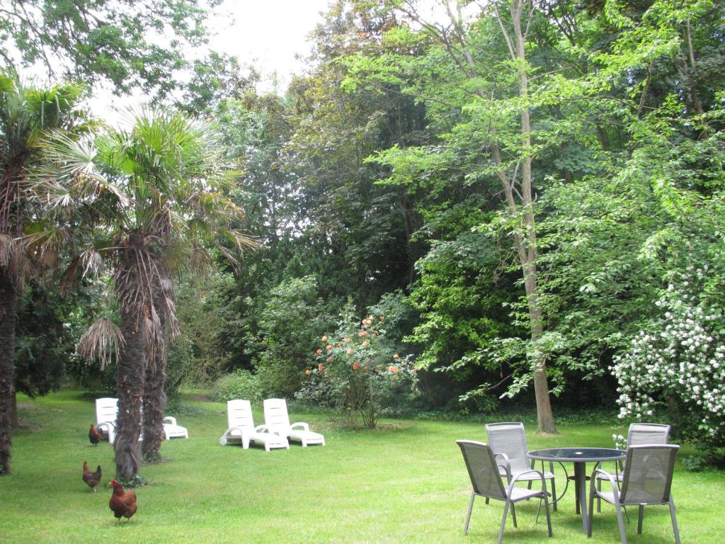 a table and chairs in a yard with chickens in the grass at Manoir de la Marjolaine in Cabourg