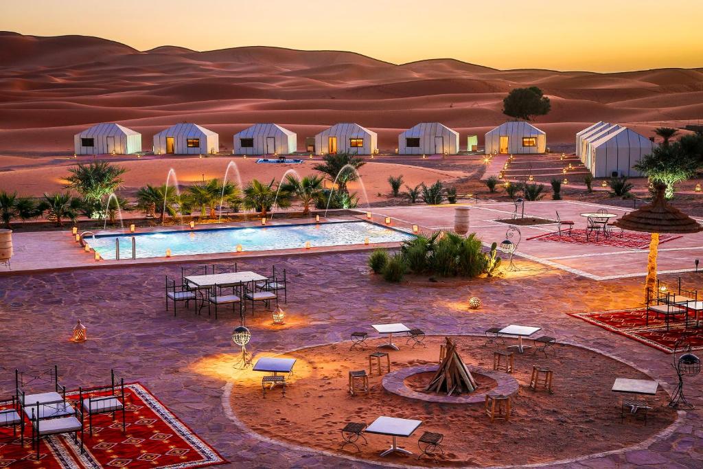 Ein Resort in der Wüste mit Pool und Tischen in der Unterkunft Yakout Merzouga Luxury Camp in Merzouga