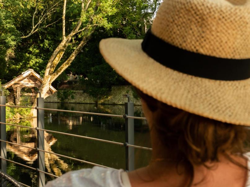 Eine Frau mit einem Strohhut, die über einen Fluss blickt. in der Unterkunft La cabane du pêcheur - Lodges de Bonfruit 