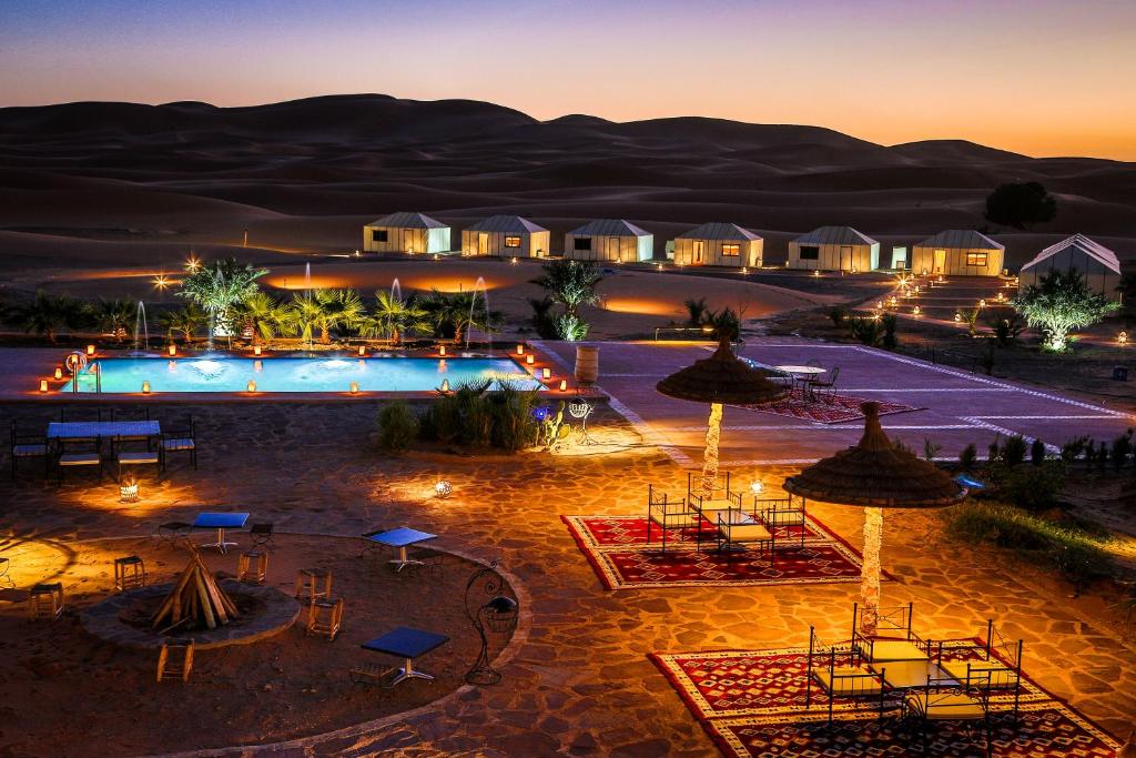 メルズーガにあるYakout Merzouga Luxury Campのリゾートで、夜はプール、テーブル、パラソルを利用できます。