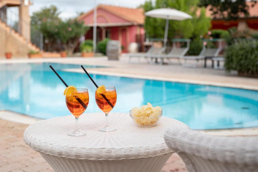 two wine glasses sitting on a table next to a pool at Ombra Verde Residence e B&B in Follonica