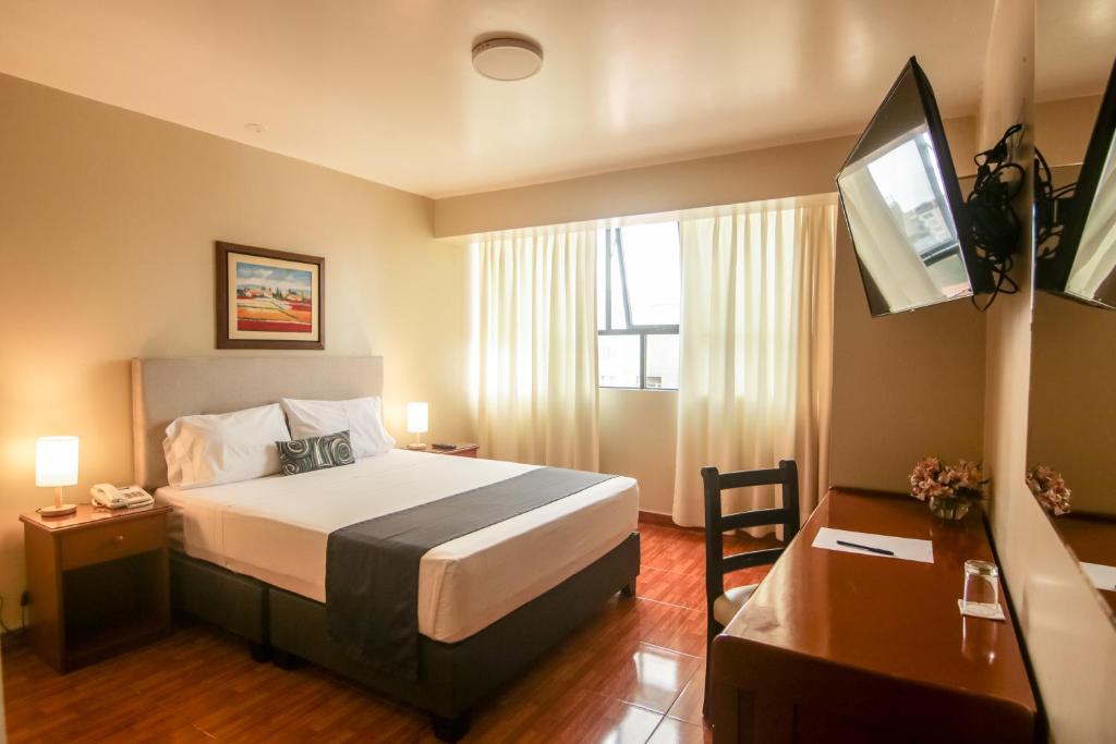 Habitación de hotel con cama, escritorio y TV. en Epiqus Hotel, en Lima