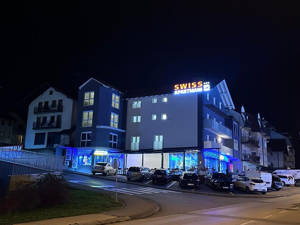 budynek z samochodami zaparkowanymi na parkingu w nocy w obiekcie Swiss Apartmani w mieście Banja Luka
