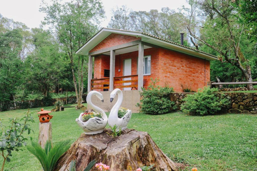 two swans sitting on a tree stump in front of a house at Pousada do Bosque Bento in Bento Gonçalves