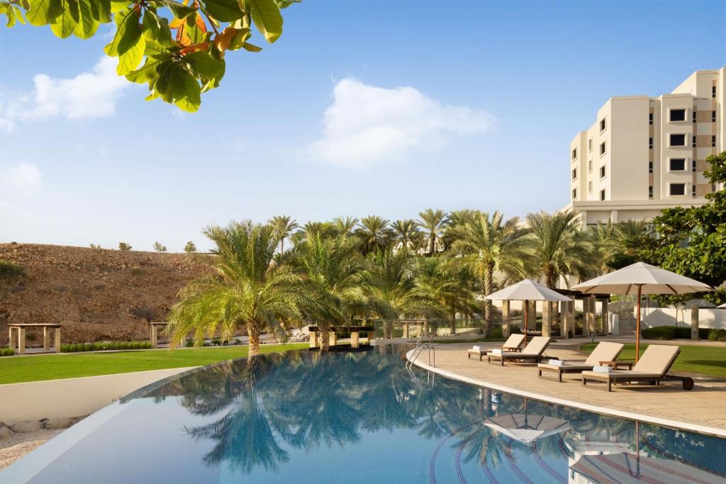 einen Pool in einem Resort mit Stühlen und Palmen in der Unterkunft JW Marriott Hotel Muscat in Muscat