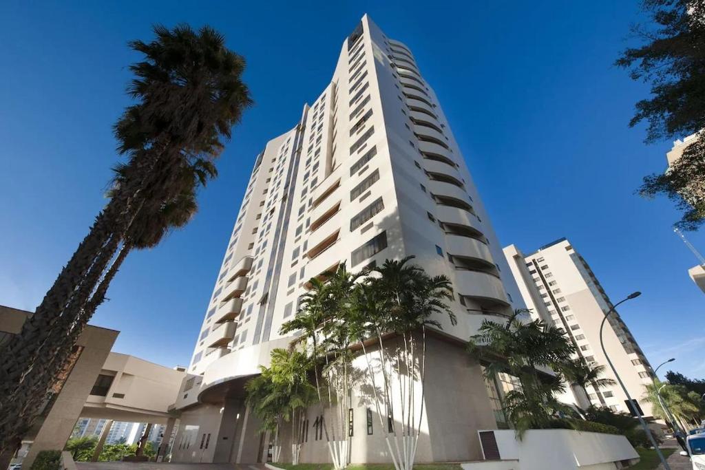 a tall white building with palm trees in front of it at Flat Particular no Comfort Suites in Brasilia