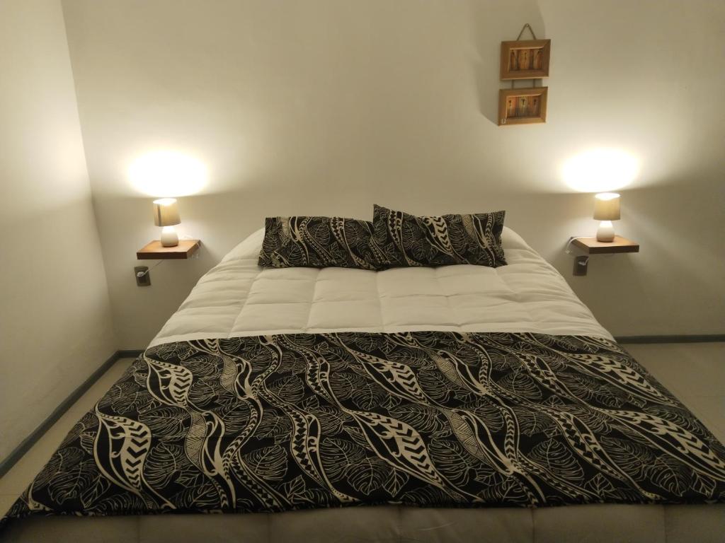 a bed with a black and white comforter and two lamps at Hotel Hanau'eepe in Hanga Roa