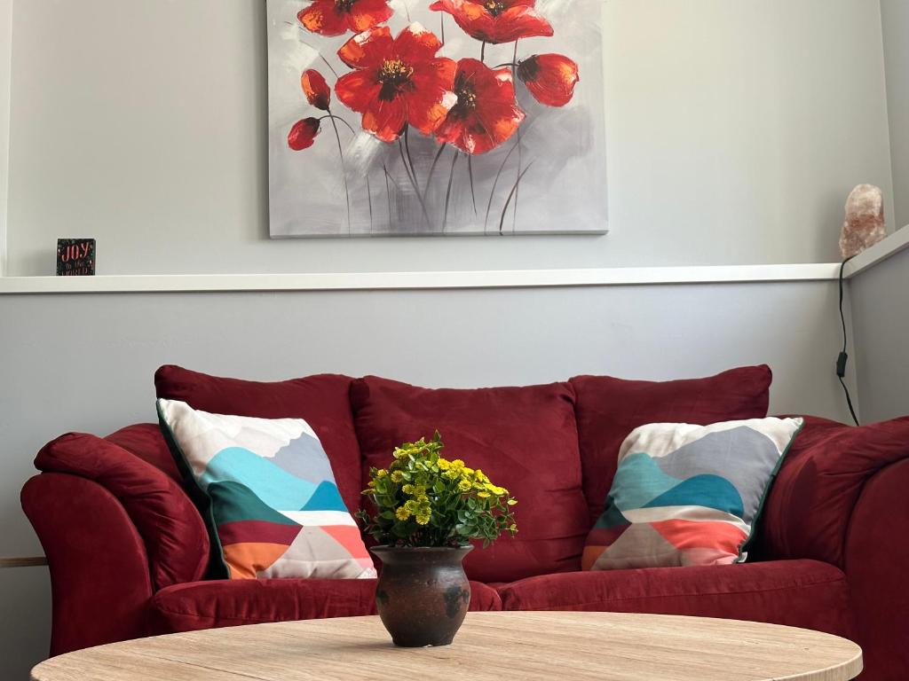 eine rote Couch mit einem Tisch und eine Vase mit Blumen drauf in der Unterkunft Exquisite Cozy Suite/full amenities in Kensington in Saskatoon