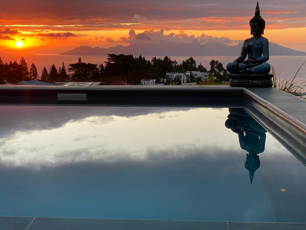 un buddha sentado en el borde de una piscina con una puesta de sol en Teanuhe Hills, en Faaa