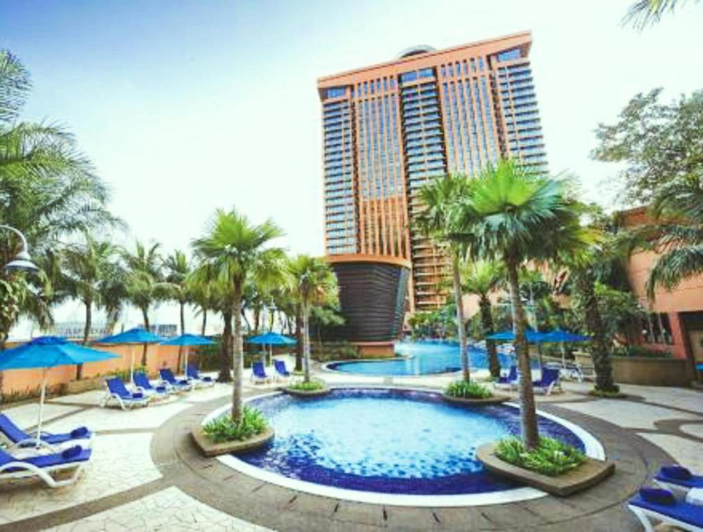 a resort pool with chairs and palm trees and a tall building at Vacation Suites at Times Square KL in Kuala Lumpur