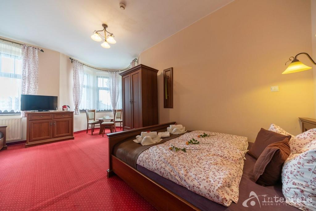 Bright hotel bedroom with wooden double bed, floral bedding, wardrobe, small seating area and TV.