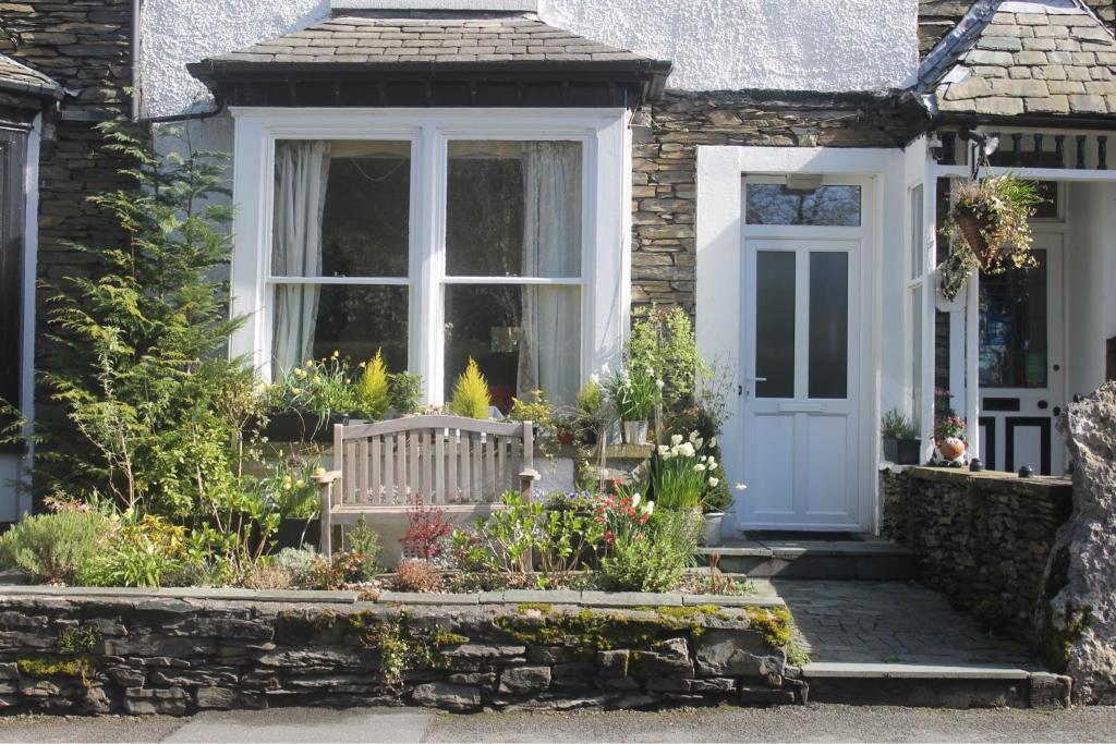 a cottage with a white door and some flowers at Birch Tree House in Windermere