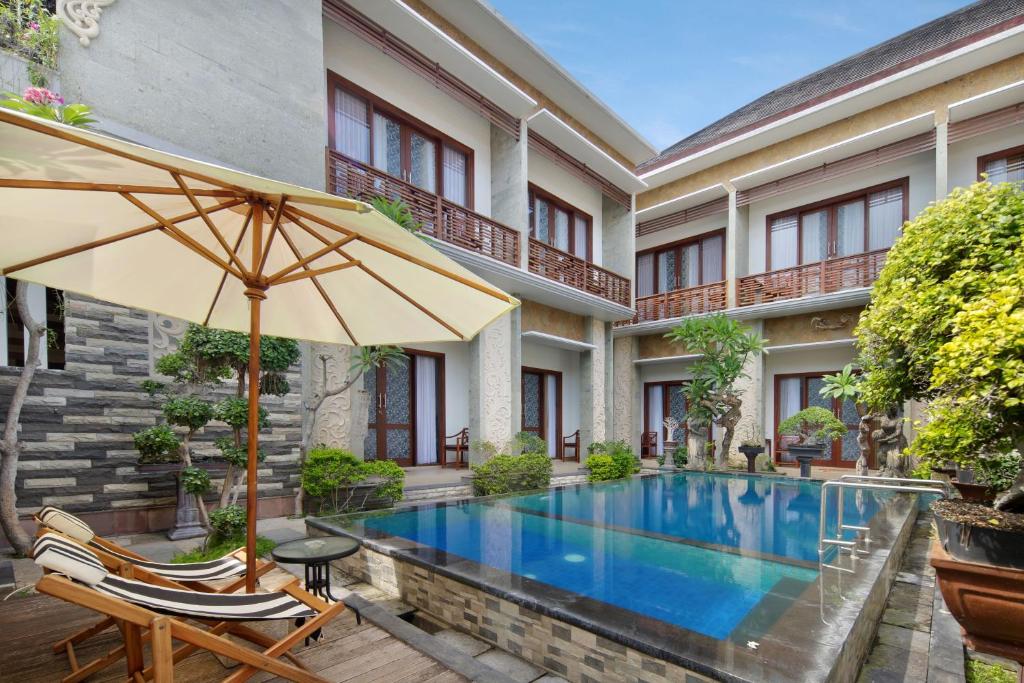 an outdoor swimming pool with an umbrella and two chairs and a table at Jineswari Kuta by Kamara in Kuta