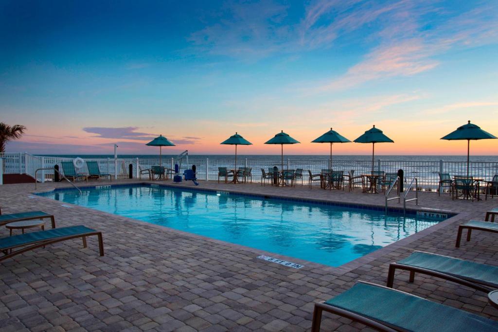 una piscina con mesas y sombrillas en un edificio en SpringHill Suites by Marriott New Smyrna Beach, en New Smyrna Beach