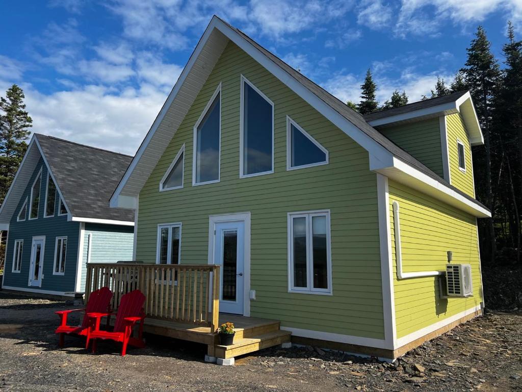a green and yellow house with red chairs on the porch at Bambury's Hillside Chalets in Rocky Harbour