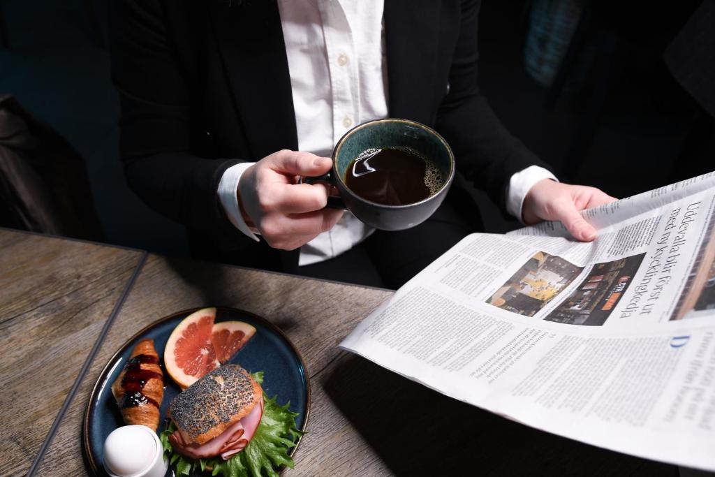Un uomo sta leggendo un giornale con un piatto di cibo di Quality Hotel Carlia a Uddevalla