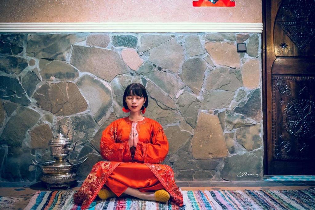 Una donna seduta sul pavimento di fronte a un muro di pietra di Riad Chay & Boutique a Ouarzazate