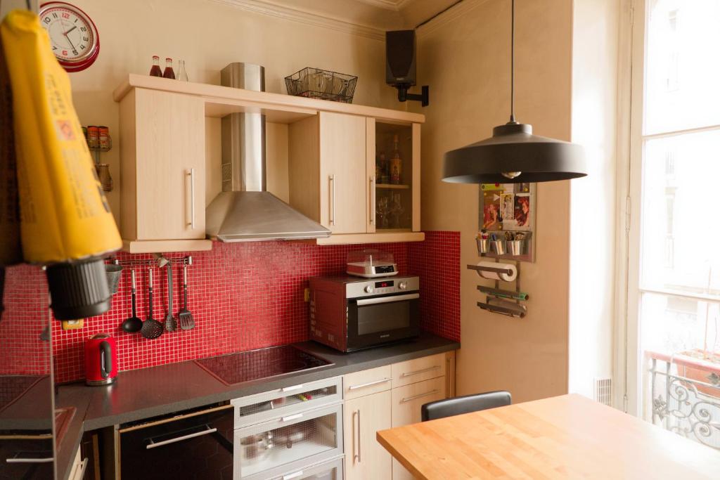 Il comprend une cuisine avec des placards blancs et un mur en carrelage rouge. dans l'établissement Paris Appartement au cœur du Marais, à Paris