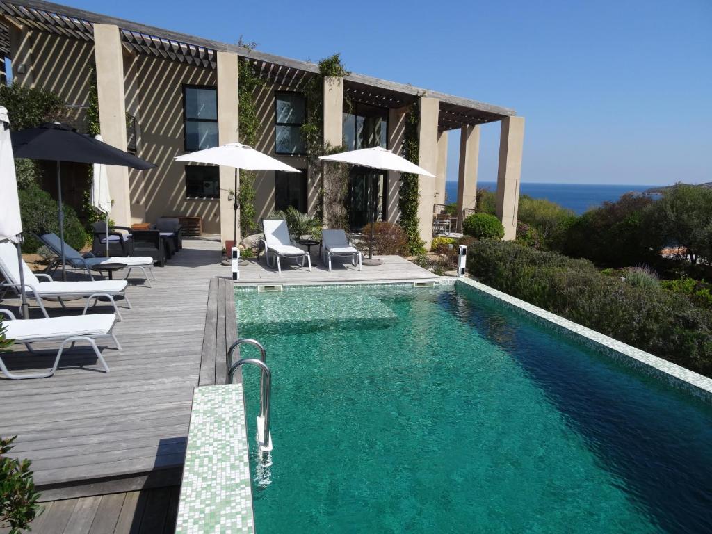 a swimming pool with chairs and umbrellas next to a building at Villa Libecciu in Sainte-Lucie de Porto-Vecchio