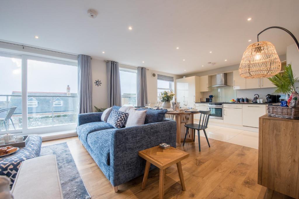 Una sala de estar con un sofá azul y una cocina. en Beautiful Central Tenby Apartment with free parking, en Tenby
