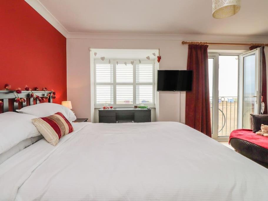 ein Schlafzimmer mit einem weißen Bett und einer roten Wand in der Unterkunft Stunning Seaviews - Beach House - Jacuzzi Bath tub in Littlestone-on-Sea
