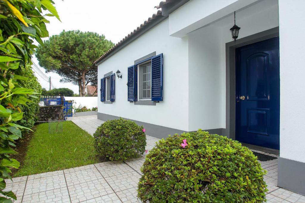 a white house with a blue door and bushes at Capelas Blue , Relax & Fun - Up to 14 Guests! in Ponta Delgada